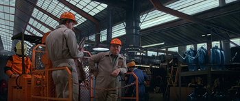 Movie still from “Heartbeeps” (1981), directed by Allan Arkush – A man wearing a hard hat in a factory; Medium shot, Low angle