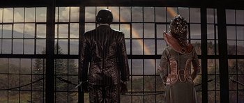 Movie still from “Heartbeeps” (1981), directed by Allan Arkush – A man and a woman standing in front of a window with a rainbow in the background; Wide shot, Low angle