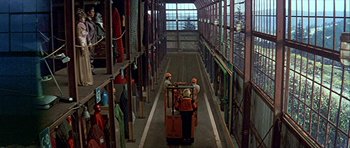 Movie still from “Heartbeeps” (1981), directed by Allan Arkush – Two men in hard hats are working in a warehouse; Extreme Wide shot, High angle