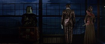 Movie still from “Heartbeeps” (1981), directed by Allan Arkush – A man in a suit standing in front of a window at night; Wide shot, Low angle