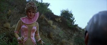 Movie still from “Heartbeeps” (1981), directed by Allan Arkush – A woman in a pink and yellow outfit standing on a hill; Medium shot, Low angle