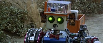 Movie still from “Heartbeeps” (1981), directed by Allan Arkush – A robot with green eyes is sitting in a field; Close Up shot, Low angle