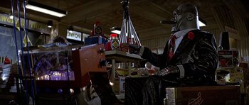 Movie still from “Heartbeeps” (1981), directed by Allan Arkush – A man sitting at a table with a lot of stuff on it; Wide shot, Low angle