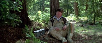 Movie still from “Heartbeeps” (1981), directed by Allan Arkush – A man sitting on the ground next to a tree; Medium shot, Low angle