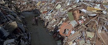 Movie still from “Heartbeeps” (1981), directed by Allan Arkush – Two people walking down a road near a pile of debris; Extreme Wide shot, High angle