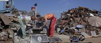Movie still from “Heartbeeps” (1981), directed by Allan Arkush – Two men working in a junk yard near a pile of junk; Wide shot, Low angle