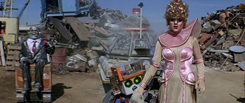 Movie still from “Heartbeeps” (1981), directed by Allan Arkush – A woman standing in front of a pile of junk; Medium shot, Low angle