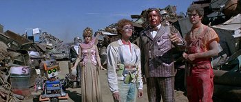 Movie still from “Heartbeeps” (1981), directed by Allan Arkush – A group of people standing next to each other on a dirt road; Wide shot, Low angle