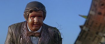 Movie still from “Heartbeeps” (1981), directed by Allan Arkush – A statue of a man wearing a hat and a bow tie; Medium shot, Low angle