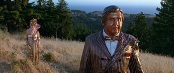 Movie still from “Heartbeeps” (1981), directed by Allan Arkush – A statue of a man wearing a suit and hat; Medium shot, Low angle