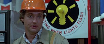 Movie still from “Heartbeeps” (1981), directed by Allan Arkush – A man wearing an orange hard hat in front of a yellow light; Close Up shot, Low angle