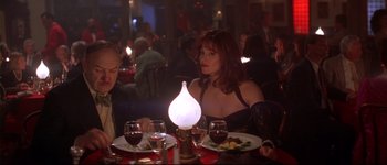 Movie still from “Heartbreakers” (2001), directed by David Mirkin – A woman sitting at a dinner table with a candle in the middle of the table; Medium shot, Over the shoulder angle