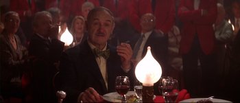 Movie still from “Heartbreakers” (2001), directed by David Mirkin – An older man sitting at a dinner table with a cigarette in his mouth; Medium shot, Low angle