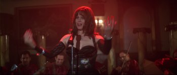 Movie still from “Heartbreakers” (2001), directed by David Mirkin – A woman in a black dress holding a microphone and waving; Medium shot, Low angle