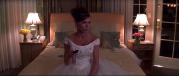 Movie still from “Heartbreakers” (2001), directed by David Mirkin – A woman sitting on a bed holding a remote control; Medium shot, High angle