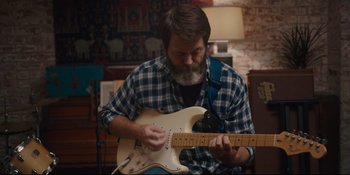 Movie still from “Hearts Beat Loud” (2018), directed by Brett Haley – A man playing an electric guitar while sitting in a chair; Medium shot, Over the shoulder angle