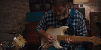 Movie still from “Hearts Beat Loud” (2018), directed by Brett Haley – A man playing an electric guitar in a room; Medium shot, Over the shoulder angle