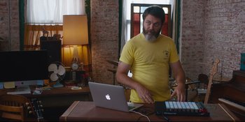 Movie still from “Hearts Beat Loud” (2018), directed by Brett Haley – A man standing in front of an apple laptop; Medium shot, Over the shoulder angle
