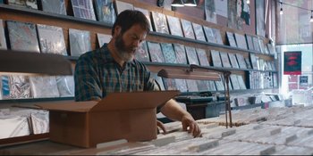 Movie still from “Hearts Beat Loud” (2018), directed by Brett Haley – A man is working in a record store; Medium shot, Over the shoulder angle