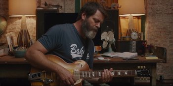 Movie still from “Hearts Beat Loud” (2018), directed by Brett Haley – A man playing a guitar in front of a fan; Medium shot, Over the shoulder angle