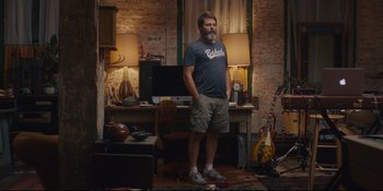 Movie still from “Hearts Beat Loud” (2018), directed by Brett Haley – A man standing next to a desk in a room; Wide shot, Low angle