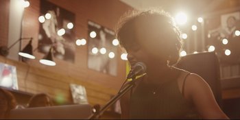 Movie still from “Hearts Beat Loud” (2018), directed by Brett Haley – A person holding a microphone in front of a microphone stand; Medium shot, Low angle