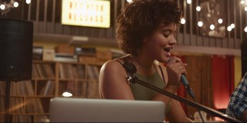 Movie still from “Hearts Beat Loud” (2018), directed by Brett Haley – A woman is singing into a microphone in front of a computer; Medium shot, Low angle