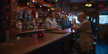 Movie still from “Hearts Beat Loud” (2018), directed by Brett Haley – A man sitting at a bar while a woman takes a picture; Medium shot, Over the shoulder angle