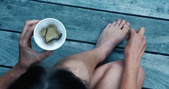 Movie still from “Hellbender” (2021), directed by Zelda Adams – A person sitting on the ground holding a cup of tea; Extreme Close Up shot, High angle