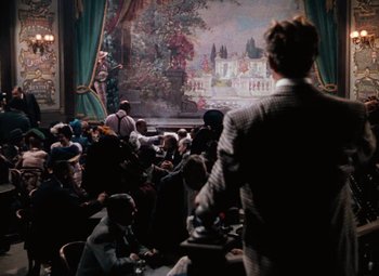 Movie still from “Hello Frisco, Hello” (1943), directed by H. Bruce Humberstone – A group of people sitting at tables in front of a painting; Wide shot, Over the shoulder angle