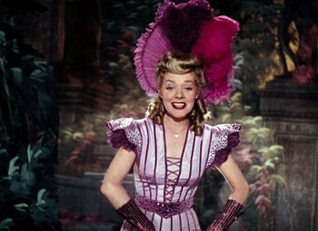 Movie still from “Hello Frisco, Hello” (1943), directed by H. Bruce Humberstone – A woman wearing a purple dress and a purple hat; Medium shot, Low angle