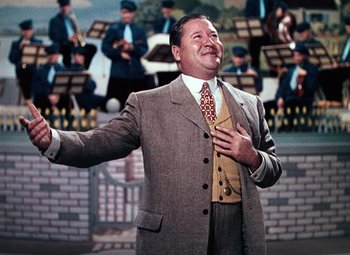 Movie still from “Hello Frisco, Hello” (1943), directed by H. Bruce Humberstone – A man in a suit and tie holding his hands to his chest; Medium shot, Over the shoulder angle