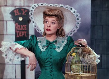 Movie still from “Hello Frisco, Hello” (1943), directed by H. Bruce Humberstone – A woman in a green dress holding a bird in a cage; Medium shot, Low angle