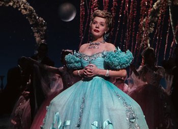 Movie still from “Hello Frisco, Hello” (1943), directed by H. Bruce Humberstone – A woman in a blue dress standing in front of a bunch of trees; Medium shot, Low angle