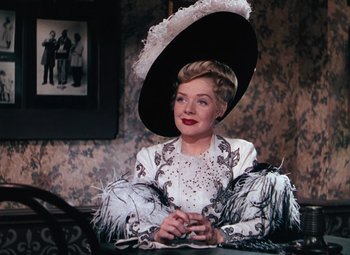 Movie still from “Hello Frisco, Hello” (1943), directed by H. Bruce Humberstone – An older woman wearing a large hat sitting on a chair; Medium shot, Over the shoulder angle