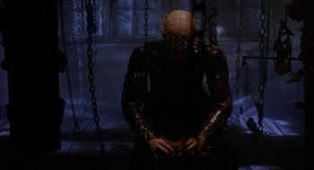 Movie still from “Hellraiser” (1987), directed by Clive Barker – A person in a black dress with a head like a pinhead; Medium shot, Low angle