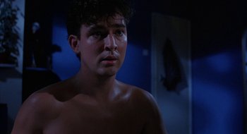 Movie still from “Hellraiser” (1987), directed by Clive Barker – A shirtless man in a dark room with a fish in the background; Close Up shot, Over the shoulder angle