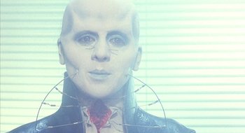 Movie still from “Hellraiser” (1987), directed by Clive Barker – A man with a bald head wearing a red tie; Close Up shot, Low angle