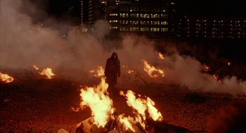 Movie still from “Hellraiser” (1987), directed by Clive Barker – A man standing in front of a fire pit at night; Extreme Wide shot, High angle