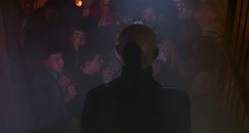 Movie still from “Hellraiser III: Hell on Earth” (1992), directed by Anthony Hickox – A person with a head piece on in front of a group of people; Medium shot, Over the shoulder angle