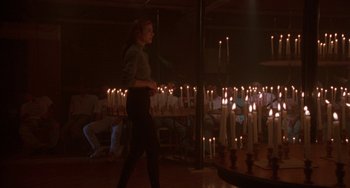 Movie still from “Hellraiser III: Hell on Earth” (1992), directed by Anthony Hickox – A woman walking in front of a bunch of candles; Wide shot, Over the shoulder angle