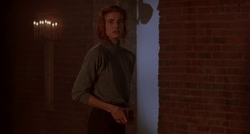 Movie still from “Hellraiser III: Hell on Earth” (1992), directed by Anthony Hickox – A woman standing next to a brick wall in a dark room; Medium shot, Over the shoulder angle