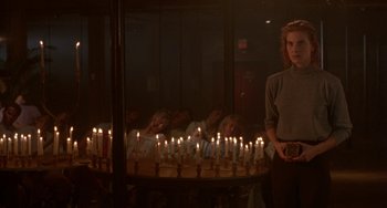Movie still from “Hellraiser III: Hell on Earth” (1992), directed by Anthony Hickox – A woman standing in front of a group of lit candles; Wide shot, Over the shoulder angle
