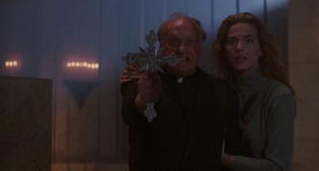 Movie still from “Hellraiser III: Hell on Earth” (1992), directed by Anthony Hickox – A priest holding a cross in front of a woman; Medium shot, Low angle