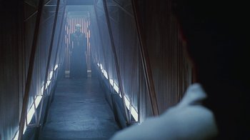 Movie still from “Hellraiser: Bloodline” (1996), directed by Kevin Yagher – A person standing in a dark hallway with a light shining on them; Wide shot, Over the shoulder angle