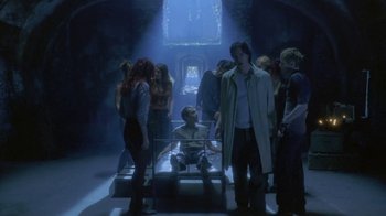 Movie still from “Hellraiser: Deader” (2005), directed by Rick Bota – A group of people standing around a man in a room; Wide shot, High angle