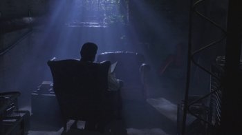 Movie still from “Hellraiser: Deader” (2005), directed by Rick Bota – A man sitting in a chair reading a book in a dark room; Wide shot, Low angle
