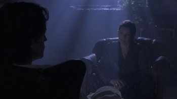 Movie still from “Hellraiser: Deader” (2005), directed by Rick Bota – A woman sitting in a chair in a room with a man; Medium shot, Over the shoulder angle