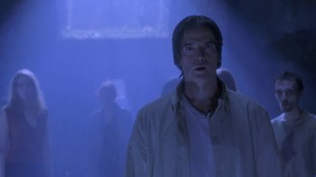 Movie still from “Hellraiser: Deader” (2005), directed by Rick Bota – A man standing in a dark room with people in the background; Medium shot, Low angle