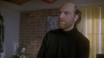 Movie still from “Hellraiser: Deader” (2005), directed by Rick Bota – A man with a beard and a black sweater is standing in front of a brick wall; Close Up shot, Over the shoulder angle